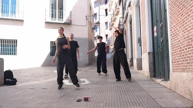 Group of talented young dancers in black outfits performing a modern hip hop choreography with synchronized movements in a narrow city street