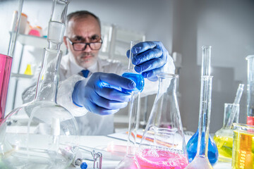Fototapeta premium Senior scientist in a white lab coat examining chemical flasks in a laboratory. Concept of classical chemistry research, scientific analysis, academic expertise and professional laboratory practice