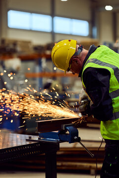 Industrial Worker Grinding Metal With Safety Helmet And High-Visibility Vest In Factory Workshop