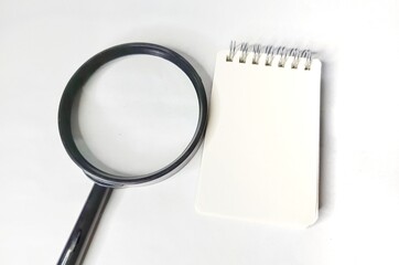 Magnifying glass and blank notebook on white background