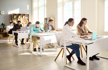 Fototapeta premium Students in classroom during training lesson. Adults work at desks with laptops, blending learning and study. Focused mood suggests exam prep. Concept of adult education and practical skills.