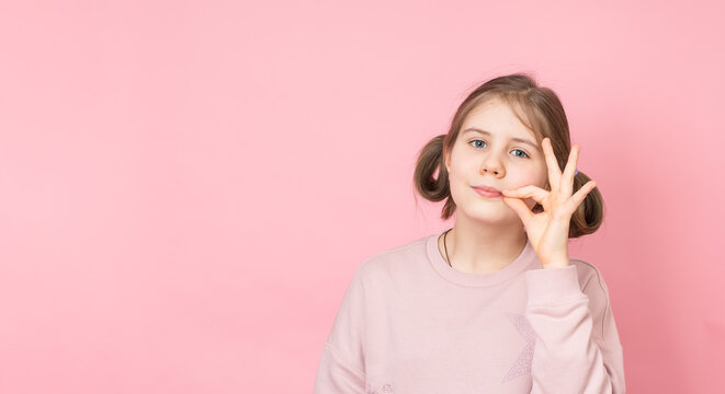 Cute preteen girl making zipper mouth gesture on pink background.
