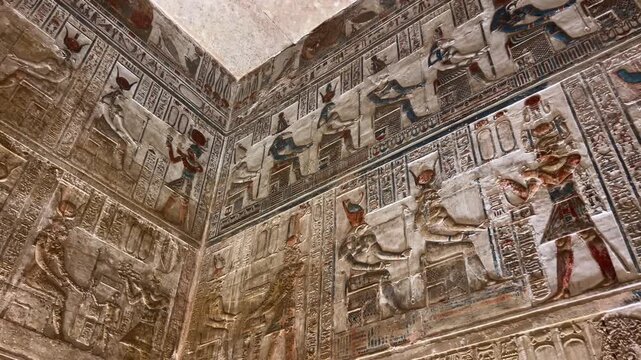 Colorful carved relief scenes on the stone walls of the Temple of Hathor at Dendera, illustrating ancient Egyptian gods, sacred rituals and daily life in richly detailed historical artwork.