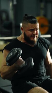 Bearded muscular athlete in a black workout outfit transitions from intense strain to a relieved smile while training on a gym bench with barbells under indoor lighting.