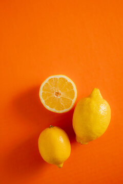 Lemons on an orange background with one lemon cut in half and two whole lemons nearby