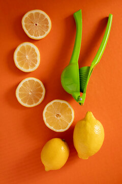 Fresh lemons and a juicer on a bright orange surface with sliced lemons arranged neatly
