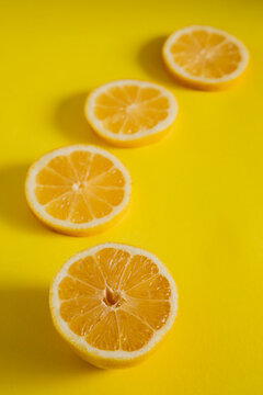 Slices of lemon arranged in a straight line on a bright yellow background in a simple kitchen setting