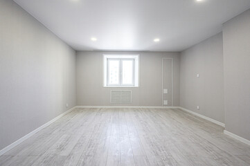 Fototapeta premium A spacious, empty room with light grey walls, wooden-style flooring, a double window, recessed ceiling lights, and a radiator beneath the window