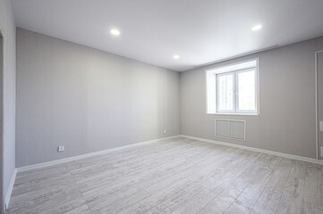 Obraz premium A spacious, empty room with light grey walls, wooden-style flooring, a double window, recessed ceiling lights, and a radiator beneath the window