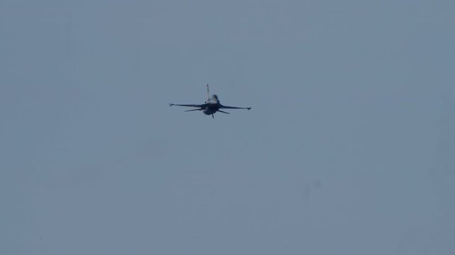 LUQA, MALTA - SEPTEMBER 28, 2025: An F-16 fighter jet flies towards the camera, releases flares, and performs a dramatic pull-up maneuver, leaving white smoke trails against a clear blue sky. Slow