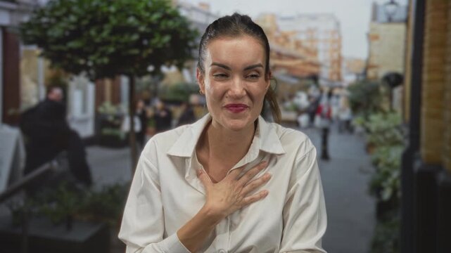 Young hispanic woman wearing white shirt with hand on chest and joyful smile in city street; gratitude.