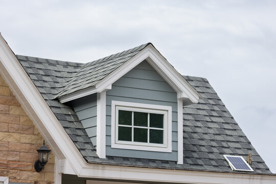 A house with a slanted roof and a window on the top. garret house with roof shingle with cloudy in rainy season. Dormer windows on the sloped shingle roof.