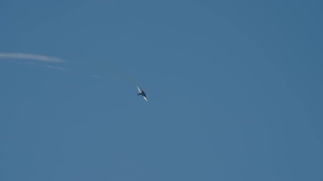 LUQA, MALTA - SEPTEMBER 28, 2025: This video footage shows a powerful military fighter jet performing high-speed aerobatic maneuvers against a clear, solid blue sky. The aircraft leaves vapor trails