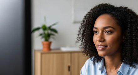 Curious Young Woman with Curly Hair Focused on Screen in Modern Office