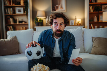 Man intently watching football, holding soccer ball and betting slip © Dusan