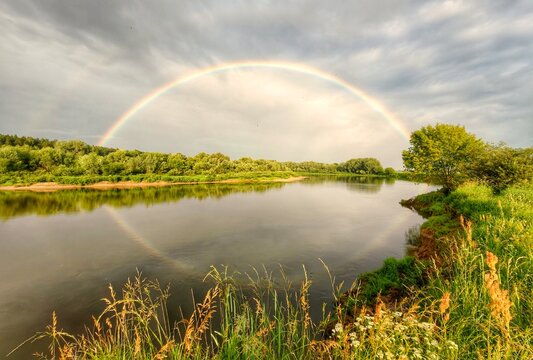 Regenboog boven rustige rivier met weerspiegeling