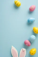 Fototapete Rund Restaurant Happy Easter vertical greeting featuring pastel decorated eggs and bunny ears arranged on a soft blue background for seasonal celebration and spring decor  © ActionGP