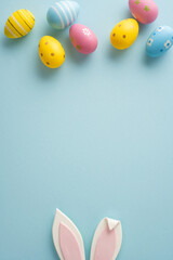 Fototapeta premium Pastel vertical decorated Easter eggs and bunny ears on a soft blue background conveying a happy Easter celebration and greeting