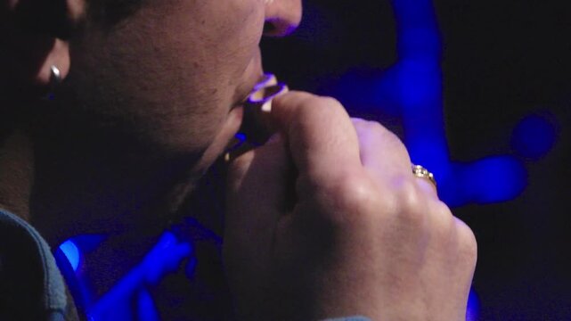 Horizontal extreme close-up focusing on a musician's mouth and hand while playing a traditional Andean pan flute (zampona). The shot captures the detail of the wooden pipes and the performer's grip