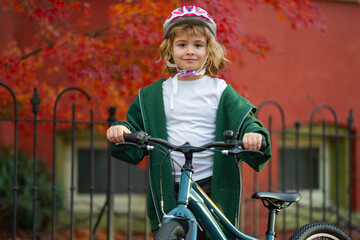 Naklejka premium Child rides bike on autumn. Kid wearing bike helmet. Happy child learning to bike ride. Child with bicycle in autumn fall park. Kid rides bike in autumn.