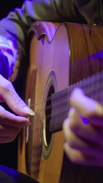 Vertical close-up focusing on a musician's right hand as they play a Colombianh stringed instrument Tiple. The image emphasizes the long, groomed fingernails used for fingerstyle technique.
