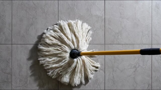 Close-up of a mop cleaning textured tiles with a focus on the mop head and the handle being held, highlighting the cleaning process