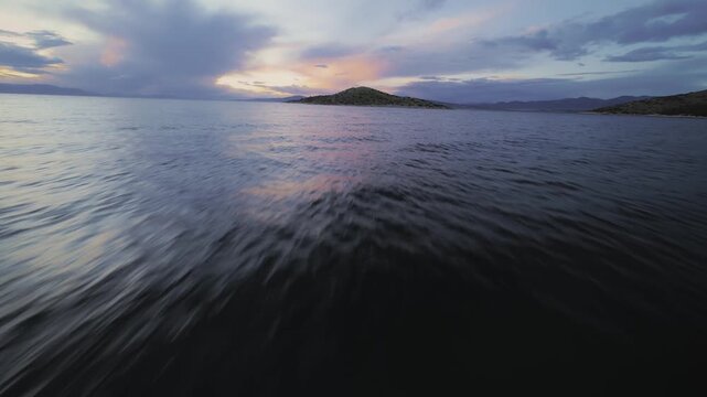Cinematic FPV drone flight very close above the sea surface during golden sunset, approaching a small island on the horizon. Smooth low altitude flight over calm water with warm sunlight reflections 