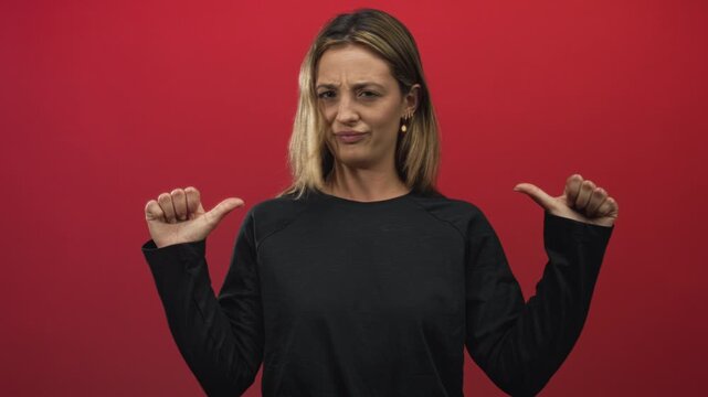 Blonde woman points both thumbs to chest in red studio with skeptical expression and raised eyebrows; skepticism.