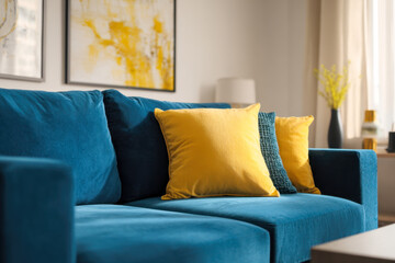 Fototapeta premium Modern living room featuring a plush blue sofa adorned with vibrant yellow and textured blue cushions under abstract yellow and white wall art for cozy ambiance