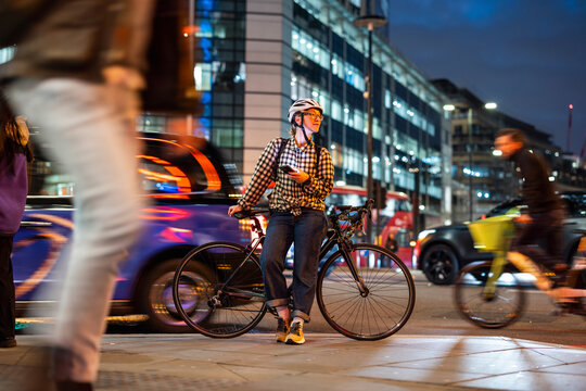 Woman with bicycle waiting on city street in London at night