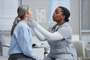 Black female young adult healthcare professional examining lymph nodes and neck of Caucasian middle...