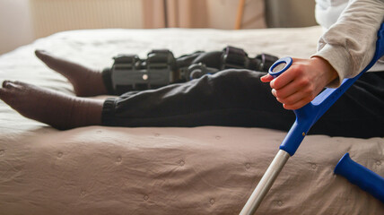 Person with leg brace and crutches sitting on a bed recovering from injury