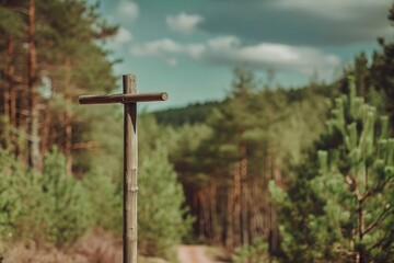 A simple wooden cross stands tall in a pine forest, marking a serene path with a gentle sky and rolling green hills in the distance.