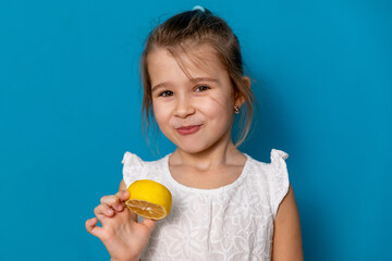 Funny little child girl try to taste fresh lemon, wrinkles and makes a grimace. Sour taste, facial...