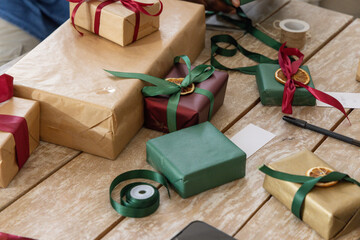 Person's hands wearing grey long-sleeve top tying green ribbon around kraft gift on wooden table