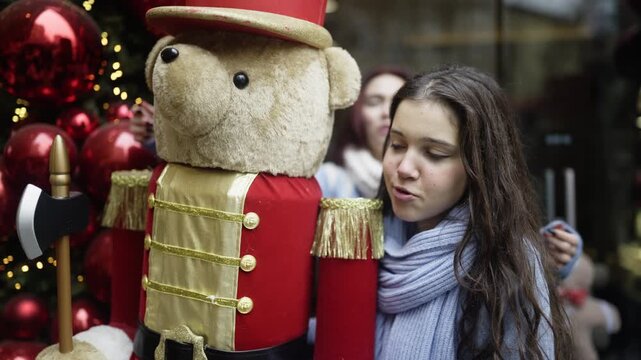 Young friends admire a festive Christmas nutcracker display during the holiday season. The girls enjoy the joyful winter decorations together on a city street.