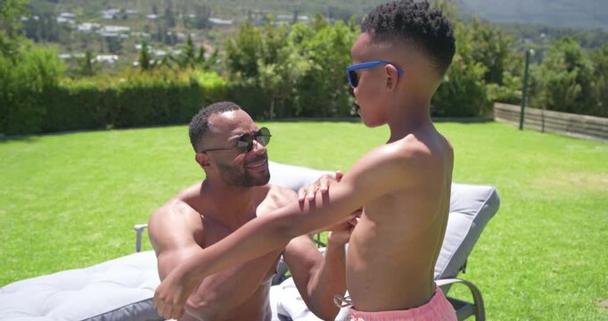 African American father and son in yard, father rubbing sunscreen on son's arms protecting from sun