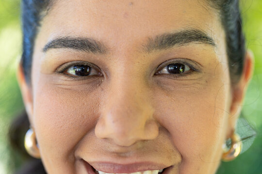 Female smiling and facing camera in garden showing gold hoop earrings and eye catchlights