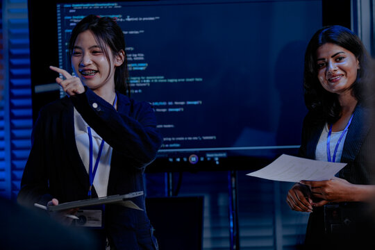 An Indian female developer leads a code review, holding a report. She explains a Python script for an AI or cybersecurity system to her team in a dark SOC Security Operations Center
