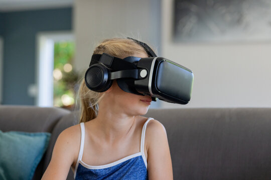 Teenage girl sitting on gray sofa wearing black VR headset and headphones and blue top
