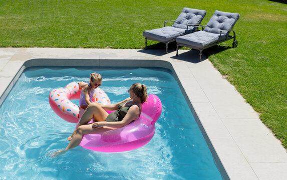 Woman and youth girl floating in rectangular in-ground pool on pink lounge and sprinkles donut