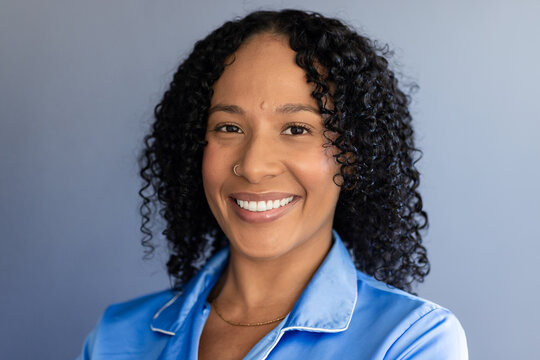African American woman smiling on studio blue backdrop in blue top white-trim gold chain nose hoop
