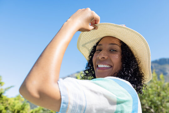African American woman smiling, holding brim of wide-brimmed straw hat outdoors with striped shirt