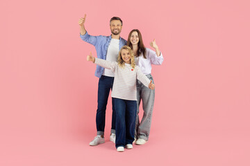 Cheerful caucasian family showing thumbs up on pink studio background, expressing approval and positivity in bright lifestyle portrait with smiling faces