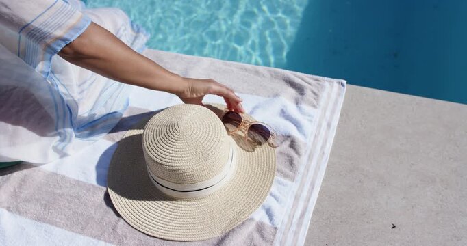 African American woman fixing coverup picking shades from towel with straw hat at pool shading eyes