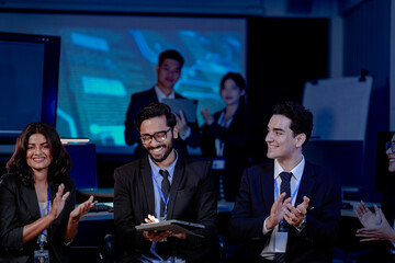 Obraz premium An Indian man with a tablet leads a discussion with his diverse colleagues, including an Indian woman, Caucasian woman, and Caucasian man. They sit in a modern tech office for a strategy meeting.