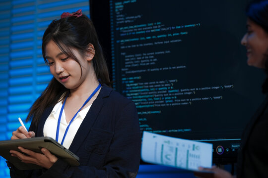 An Indian female developer leads a code review, holding a report. She explains a Python script for an AI or cybersecurity system to her team in a dark SOC Security Operations Center.