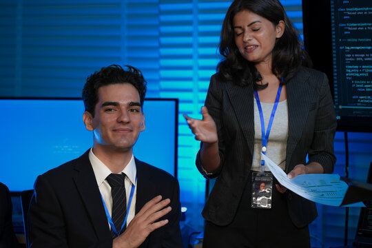 An Indian female developer leads a code review, holding a report. She explains a Python script for an AI or cybersecurity system to her team in a dark SOC Security Operations Center.