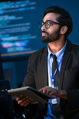 An Indian male software engineer or data scientist holds a tablet in a command center. He is asking...