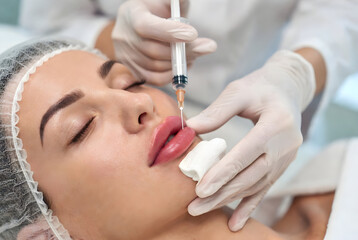 Naklejka premium Woman receiving lip filler injection from doctor in aesthetic clinic, close up of cosmetic dermatology procedure for lip augmentation and beauty enhancement